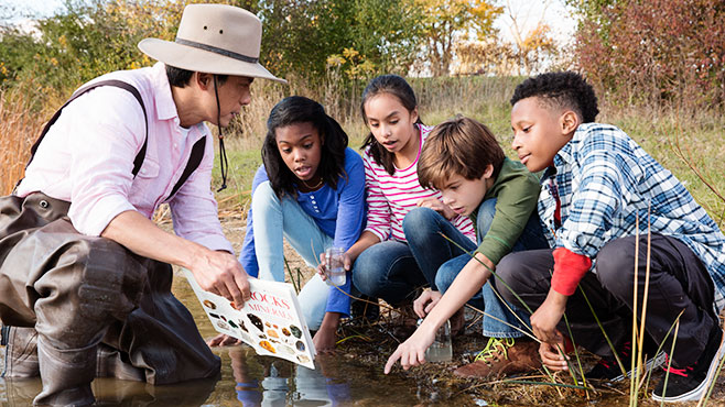 Photo of children looking at a book in a pond